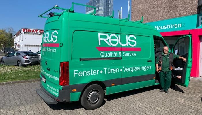 Mann-steht-in-der-Autotuer-eines-gruenen-Transporters-mit-Firmenwerbung-von-Reus-Hanau
