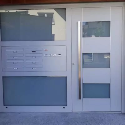 b4894662-45b0-4878-b01c-ddd6e4a061f5 hellgraue-Haustuer-fuer-Wohnungskomplex-mit-mehreren-Klingeln-und-Briefkaesten